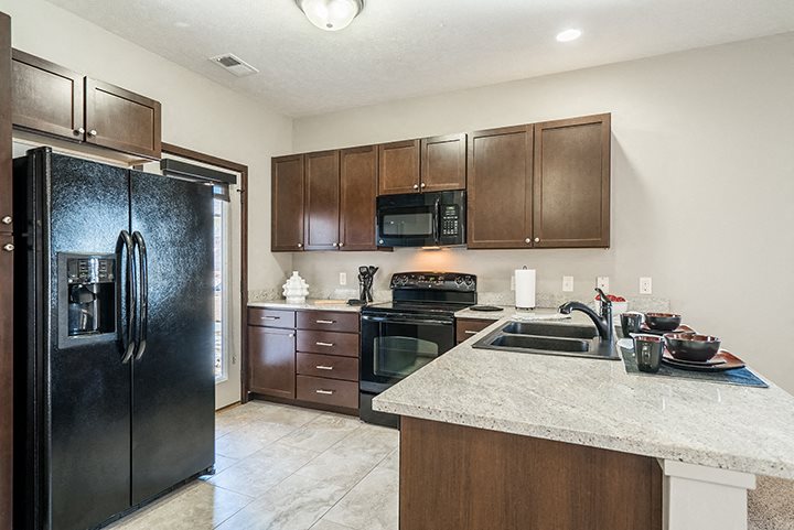 Kitchens feature dark cabinets, sleek black appliances, and gorgeous granite counter tops.